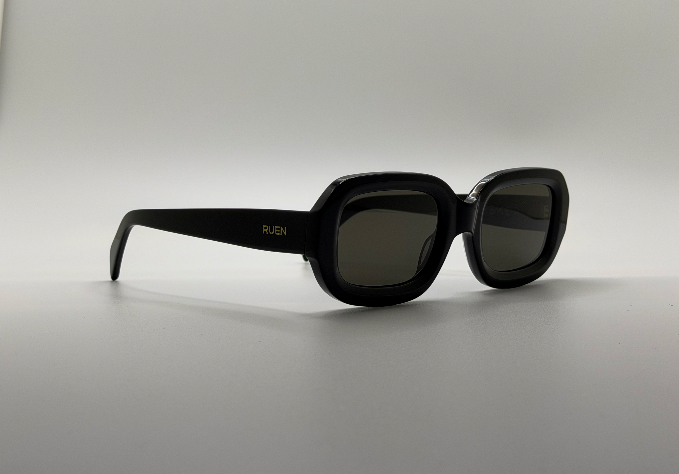 Black sunglasses with gold logo on a light gray background