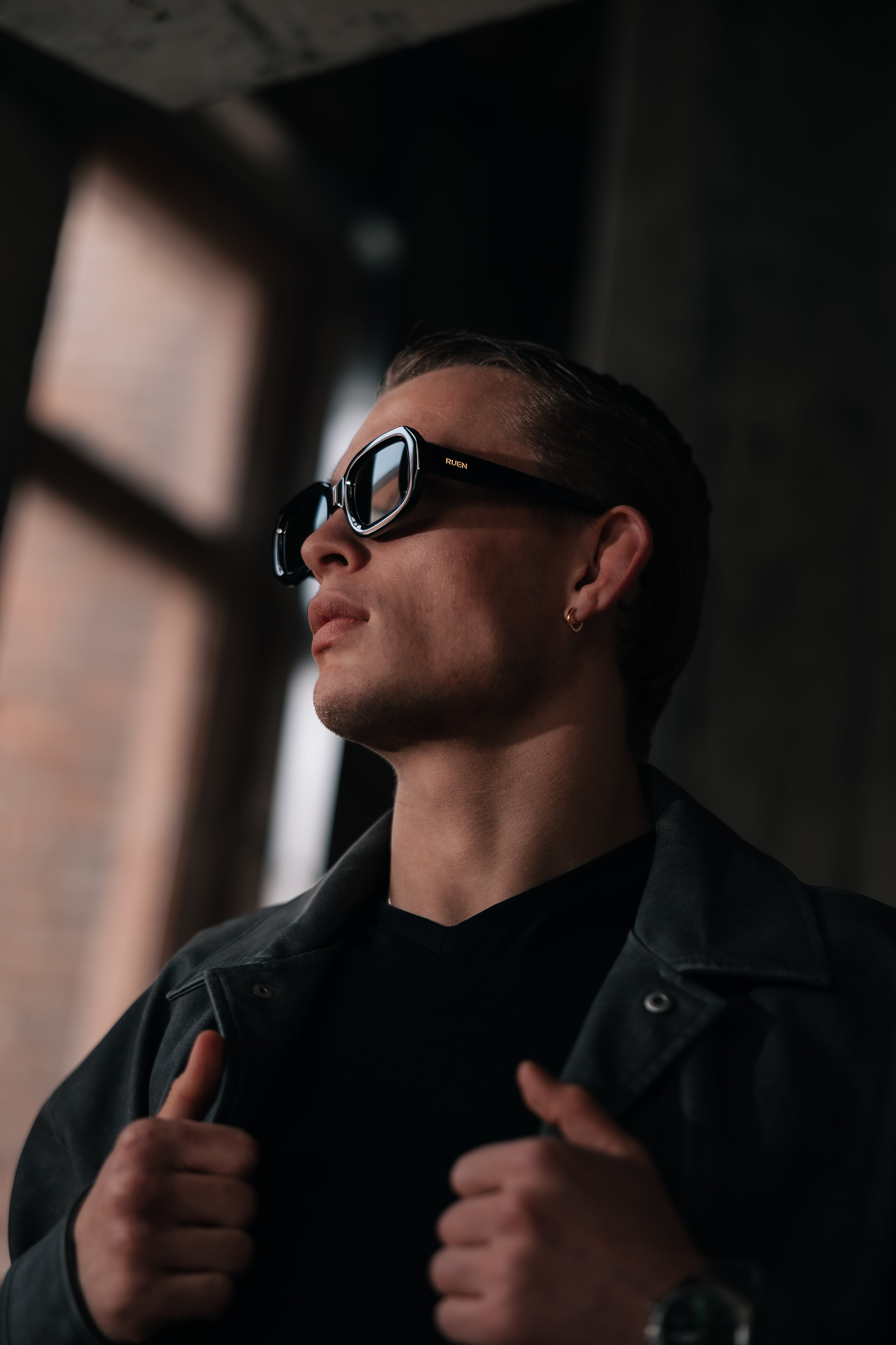 Man wearing sunglasses and a black jacket in a dimly lit room