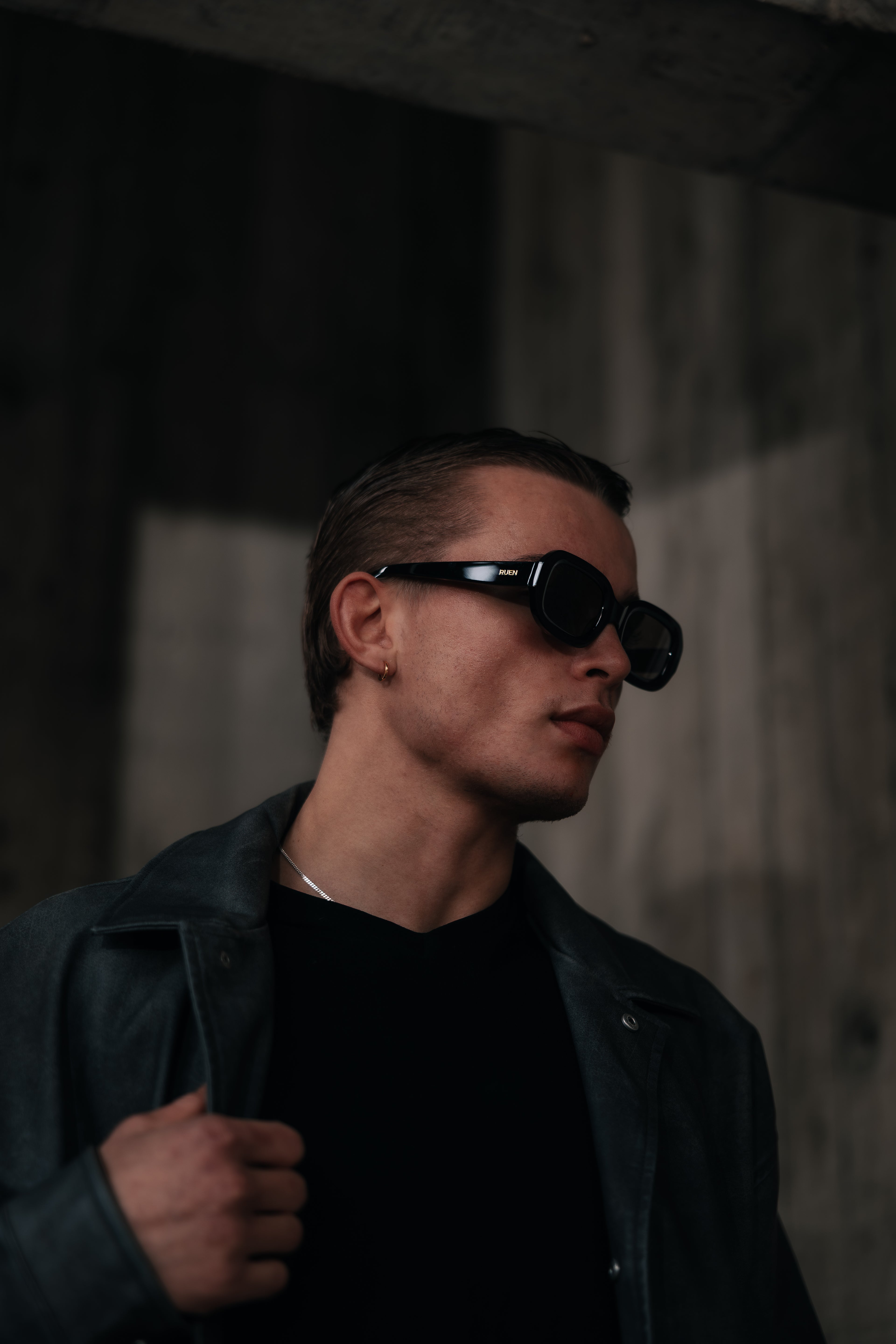 Man wearing sunglasses and a black leather jacket in a dark setting