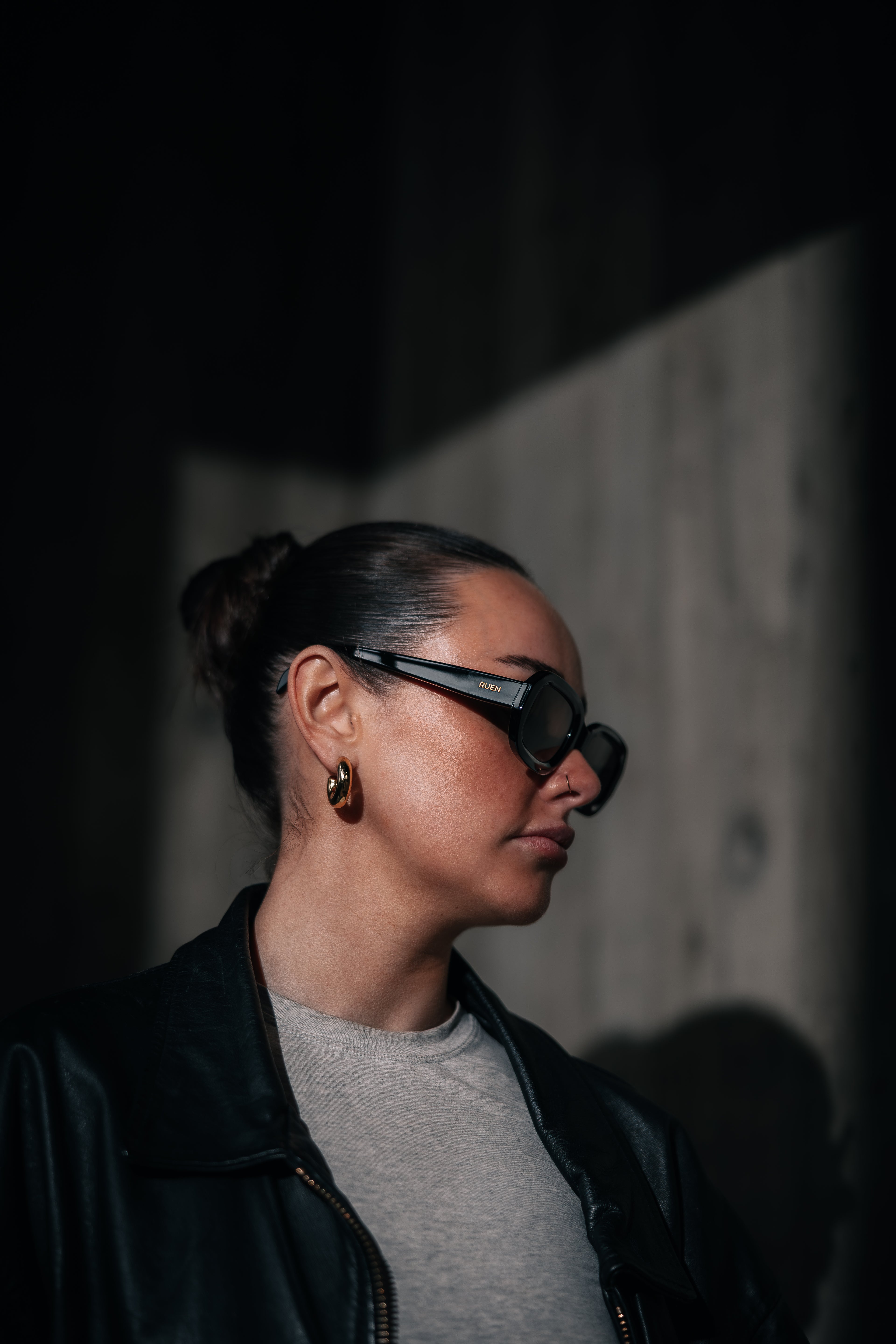 Person wearing sunglasses and a black jacket in a dimly lit setting