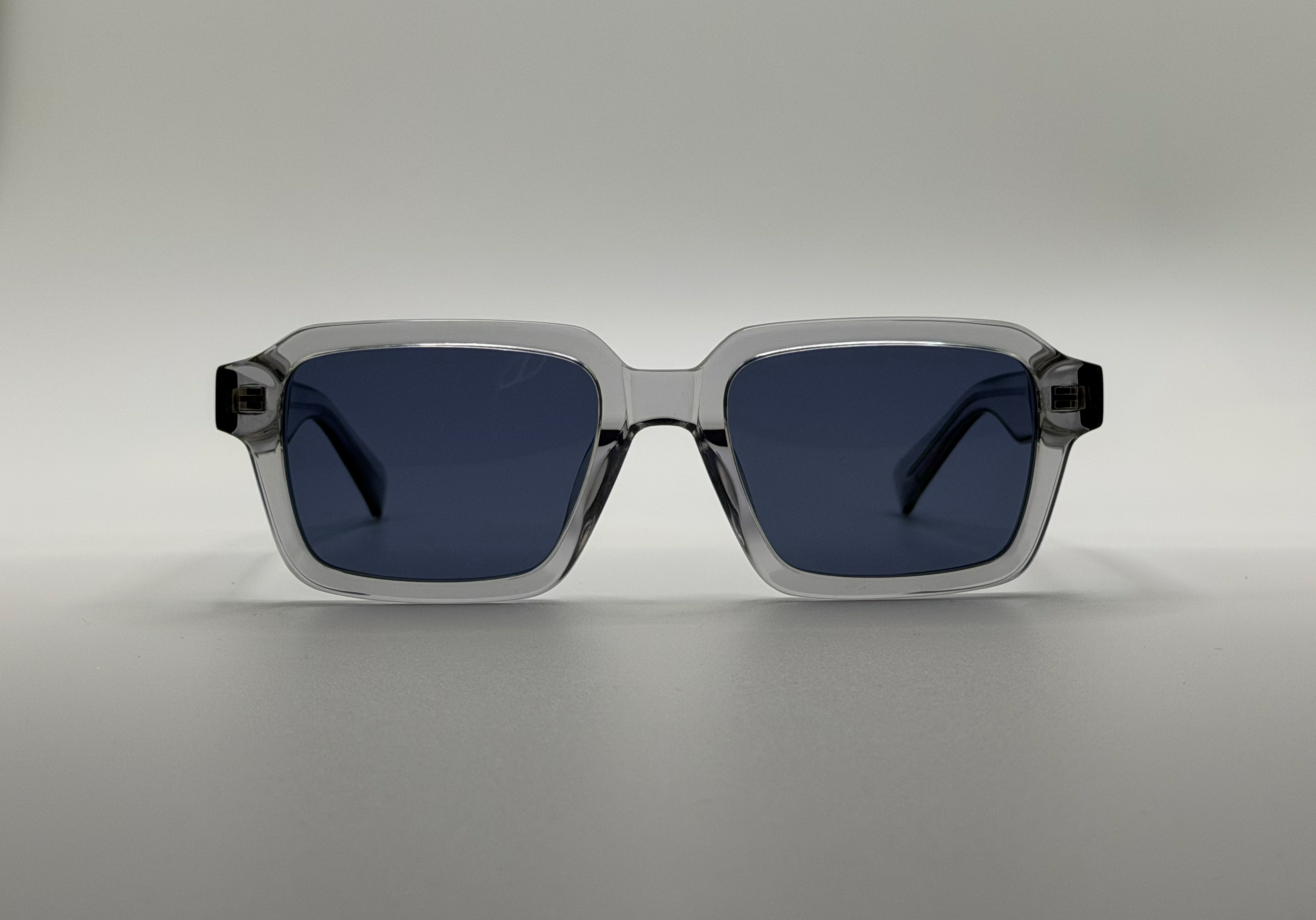 Sunglasses with a clear frame and dark lenses on a gray background