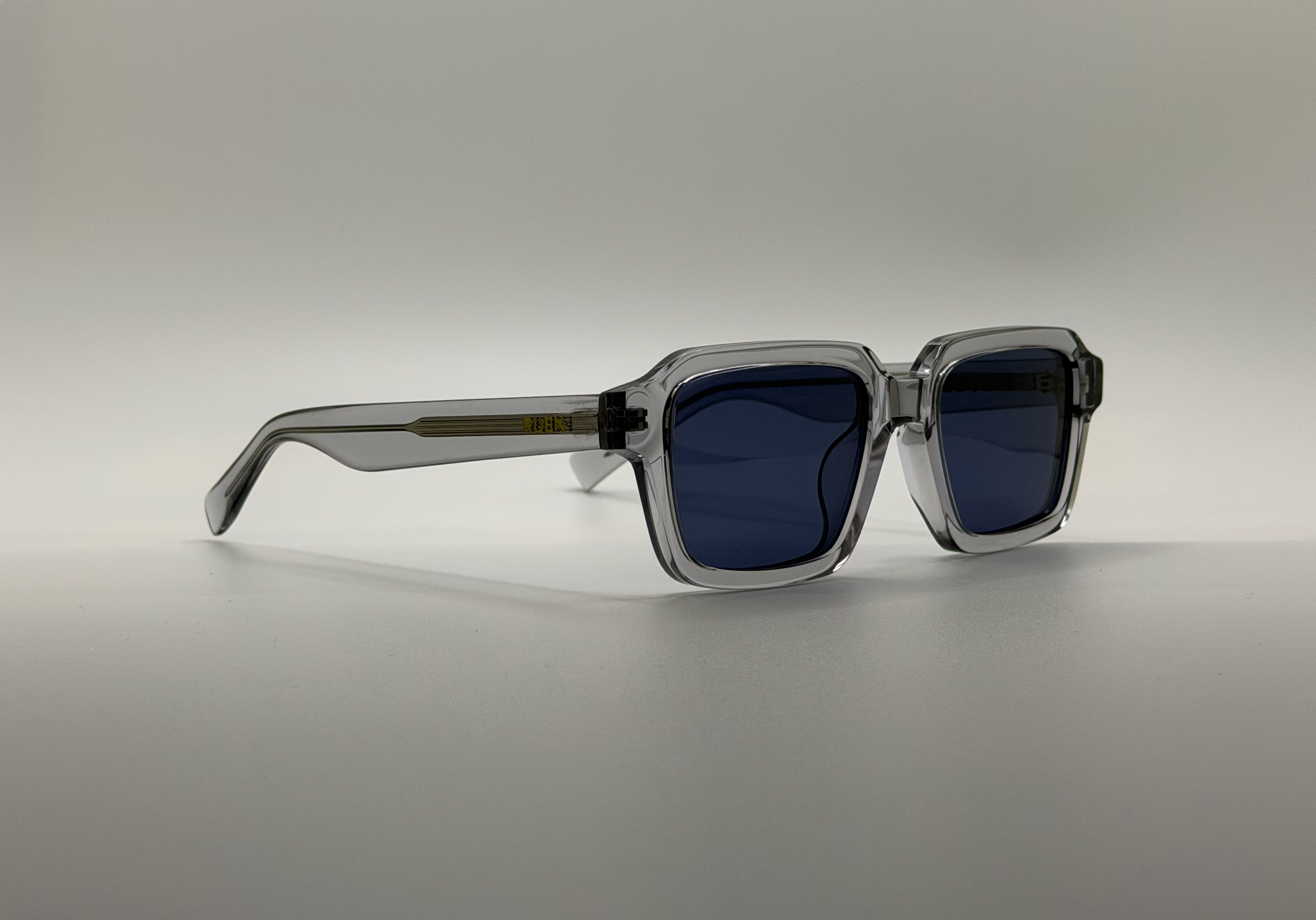 Sunglasses with clear frame and dark lenses on a light gray background