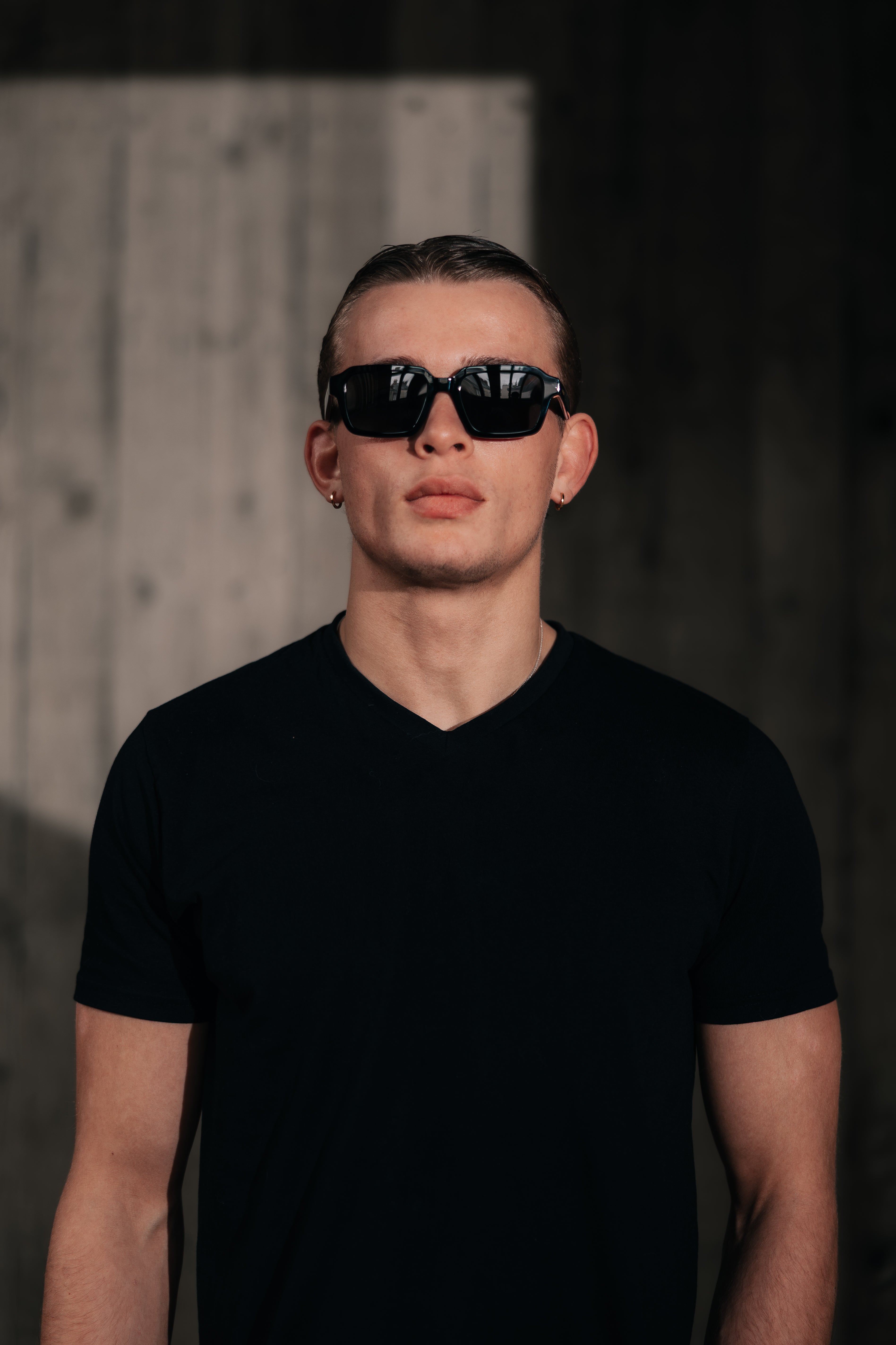 Man wearing black sunglasses and a black t-shirt against a dark background