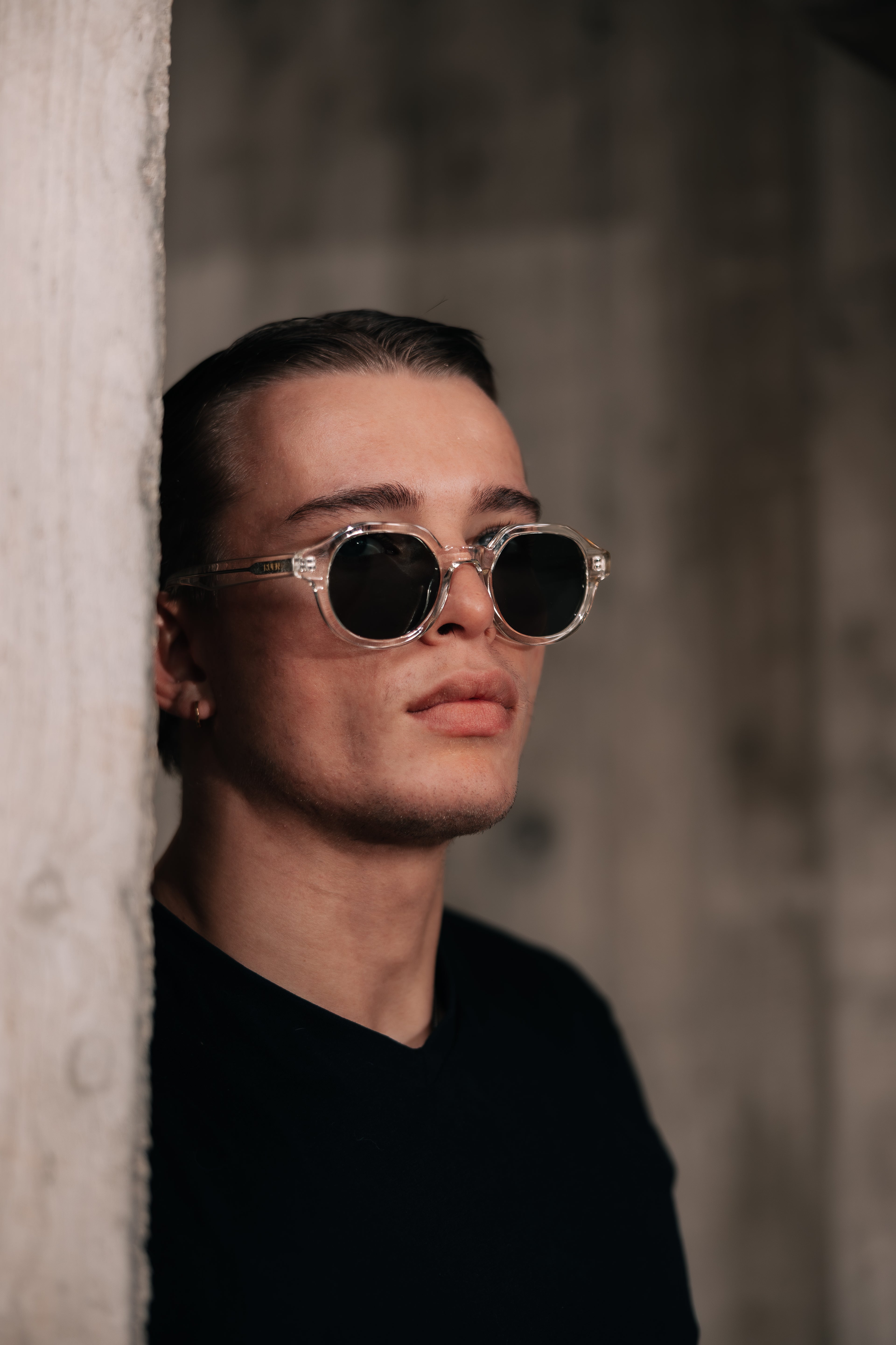 Man wearing sunglasses peeking around a corner with a blurred background