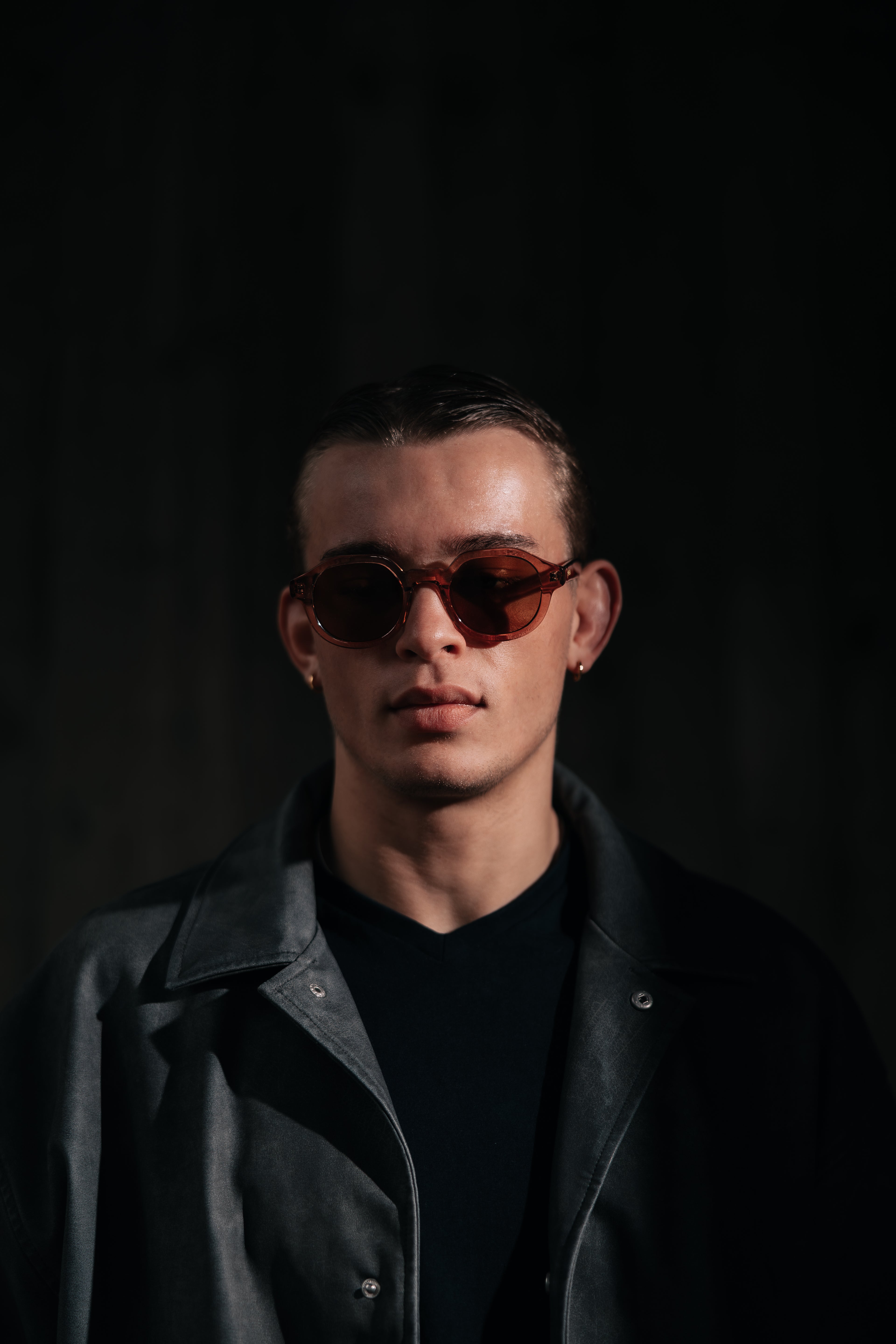 Man wearing sunglasses and a dark coat against a black background