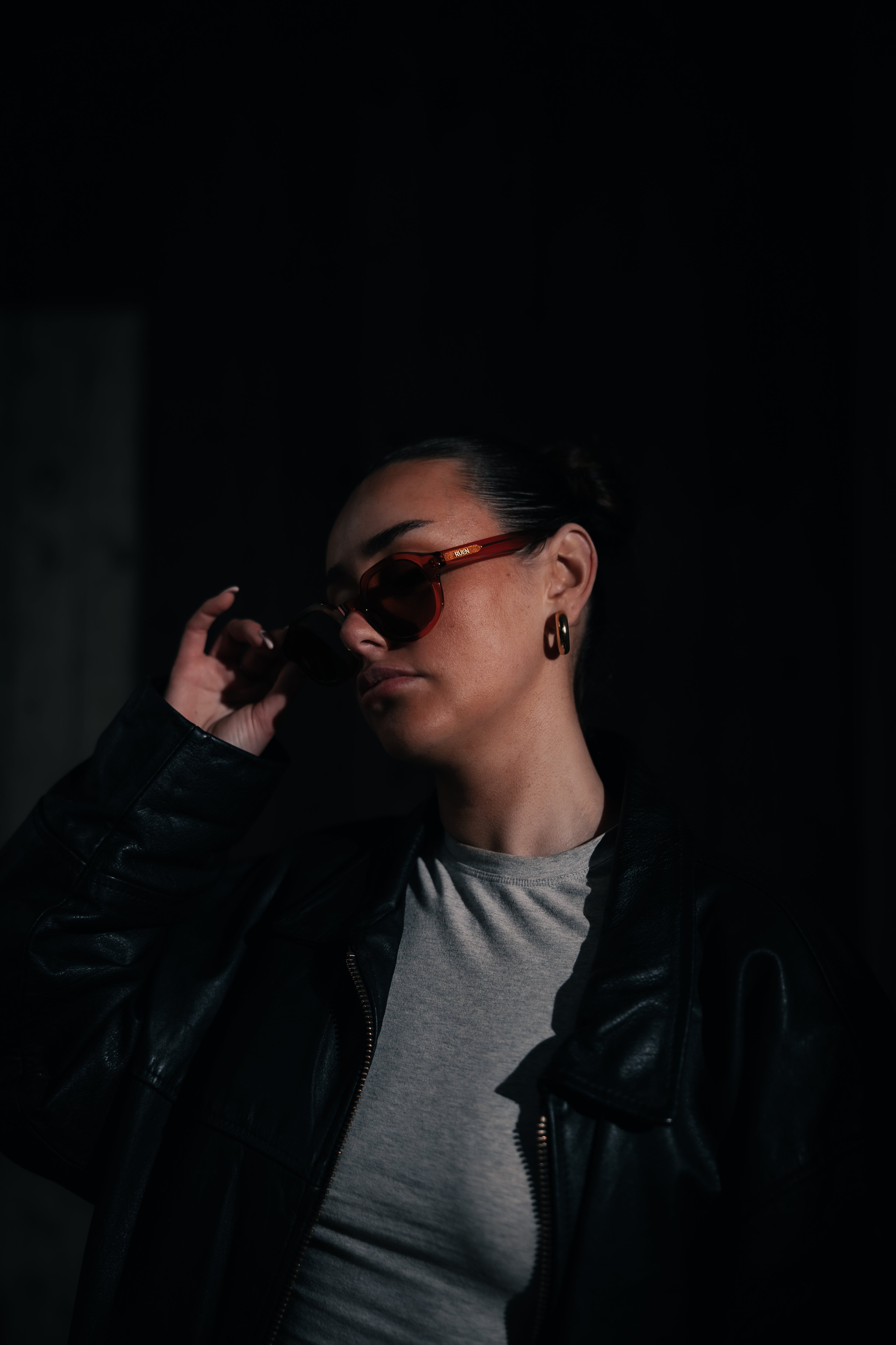 Person wearing sunglasses and a dark jacket in a dimly lit setting